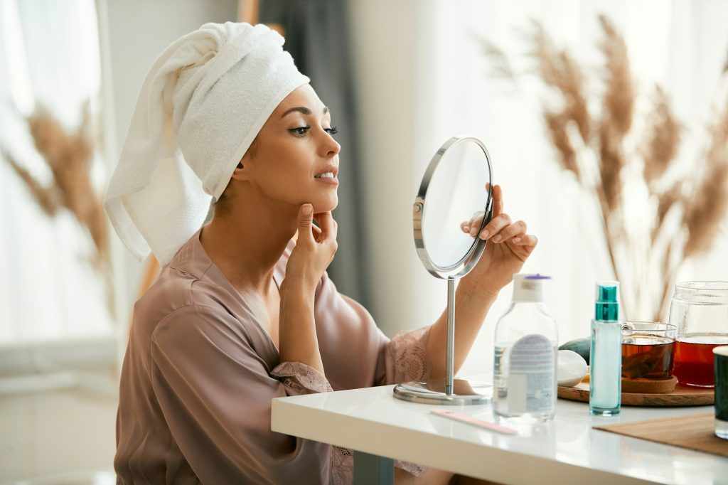 Young beautiful woman looking at her face skin in a mirror at home.